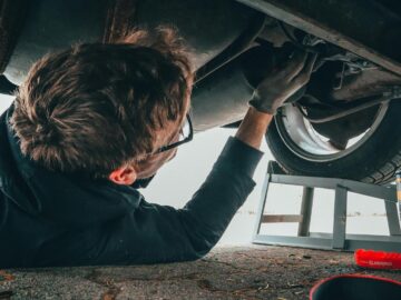 Mechanic skillfully repairing car undercarriage in outdoor setting with tools.
